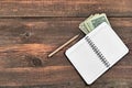 Open Notepad, Pencil And Dollars Cash On Rough Wood Background