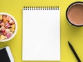 Open notepad on spiral with clean white page, cup with cocoa, caramels in a bowl, smartphone and pencil