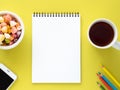 Open notepad on the spiral with a clean white page, a Cup with tea, caramels in a bowl, a smartphone and color pencil