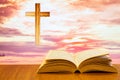 Open old bible on a wood table with blurred cross & colourful clouds and sky as background Royalty Free Stock Photo