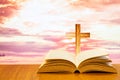 Open old bible on a wood table with blurred cross & colourful clouds and sky as background Royalty Free Stock Photo