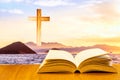 Open old bible on a wood table with blurred cross & colourful clouds and sky as background Royalty Free Stock Photo