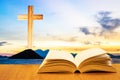 Open old bible on a wood table with blurred cross & colourful clouds and sky as background Royalty Free Stock Photo