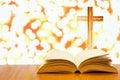 Open old bible on a wood table with blurred cross & colourful sparking lights as background