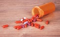 An open orange bottle of brightly coloured pills spilled onto a wooden table. Vitamin supplements are a good way to stay Royalty Free Stock Photo