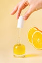 Open orange bottle with pipette in woman hand on beige background