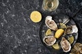 Open oysters with lemon wedges, crushed ice on a black dish on a dark stone background with oyster shells with a glass of champagn