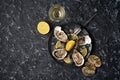 Open oysters with lemon wedges, crushed ice on a black dish on a dark stone background with oyster shells with a glass of champagn