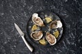 Open oysters with slices of lemon, crushed ice on a black dish with a knife for cutting oysters on a dark stone background.