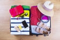 Open packed suitcase with female summer clothes and accessories, hat, sunglasses, beach towel, sunscreen and bathing suit on woode Royalty Free Stock Photo