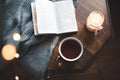 Open paper book with cup of coffee and burning candle on knit sweater on wooden table close up top view. Royalty Free Stock Photo