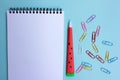 Open paper notebook with a red pen and colorful paper clips on blue background. Back to school concept. Royalty Free Stock Photo