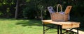 Open picnic basket on wooden table in park, space for text. Banner design