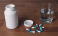 Open pill bottle with blue capsules beside a glas water. Royalty Free Stock Photo