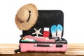 Open pink suitcase with different beach objects on wooden table