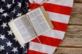 Open is reading Holy Bible book with prayer for america over ruffle American flag in wooden table