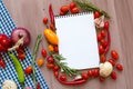 Open recipe book with fresh vegetables and herbs on wooden.