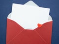 Open red envelope with blank white card and small heart on blue texture background. Royalty Free Stock Photo