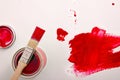 Open red paint canister on white table painted with brush