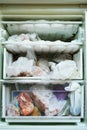 Open refrigerator with a freezer which has not been defrosted for a long time full of food and lots of frozen ice