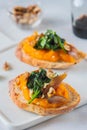 Open sandwich or bruschetta with pumpkin puree, stewed spinach and smoked fish on a white plate against a light concrete