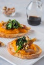 Open sandwich or bruschetta with pumpkin puree, stewed spinach and smoked fish on a white plate against a light concrete