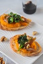 Open sandwich or bruschetta with pumpkin puree, stewed spinach and smoked fish on a white plate against a light concrete