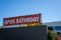 Open Saturday sign hanging on top of store building on sunny day