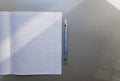 Open school notebook with pen on a gray desk with sun rays from the window. A blank, white sheet of notebook for writing. Royalty Free Stock Photo