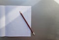 Open school notebook with pen on a gray desk with sun rays from the window. A blank, white sheet of notebook for writing. Royalty Free Stock Photo