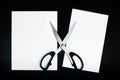 Open scissors lie on a cut sheet of A4 paper on a black background. A4 sheet of paper cut in half Royalty Free Stock Photo