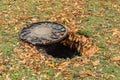 Open sewer hatch on the lawn, covered with fallen autumn leaves Royalty Free Stock Photo