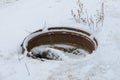 Open sewer manhole with garbage covered in snow in winter. Dangerous emergency sewer