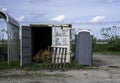 Open shipping container and a portapotty, an old wood pallet leaned up against the closed door.