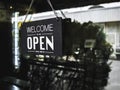 Open sign board with white text on black vintage wooden sign `Welcome we are open please come in` hanging on the glass door. Royalty Free Stock Photo