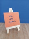 We are open sign on a wood easel on a wood and blue background