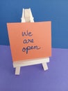 We are open sign on a wood easel on a purple and blue background