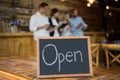 Open signboard with customers in background at coffee shop Royalty Free Stock Photo