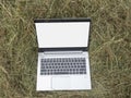 An open silver laptop is lying on a haystack. Close-up, modern technologies in rural areas. Blank screen, mockup