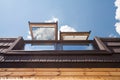 Open skylights mansard windows in wooden house with tile against blue sky.