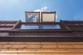 Open skylights mansard windows in wooden house with tile against blue sky.