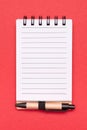 Open spiral lined paper notebook with small pen on red background Royalty Free Stock Photo