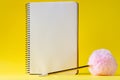 Open spiral notebook with blank empty white sheets and a golden pen with a pink fluffy ball on a bright yellow background Royalty Free Stock Photo