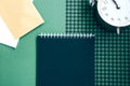 Open spiral notepad with black pages, two envelopes and vintage alarm clock on a green checkered background