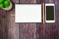 An open spiral sketchbook and mobile phone with black cover on wood table, decorate with a plant