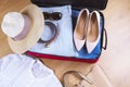 Open suitcase with casual woman clothes hat, sunglasses, white shirt, shoes, bag on wooden floor top view close up. Packing travel Royalty Free Stock Photo