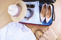 Open suitcase with casual woman clothes hat, sunglasses, white shirt, shoes, bag on wooden floor top view close up. Packing travel Royalty Free Stock Photo