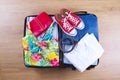 Open packed suitcase with female summer clothes and accessories, bathing suit, sneakers, white shirt on wooden floor top view