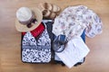 Open suitcase with casual female clothes hat, sunglasses, dress, shoes, on wooden floor top view close up. Packing travel bag for Royalty Free Stock Photo