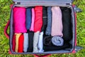 Open suitcase on the green grass with different clothes folded vertically. Vertical storage for easy travel packing